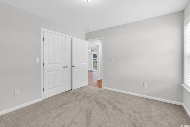 unfurnished bedroom with carpet floors, multiple windows, a closet, and baseboards