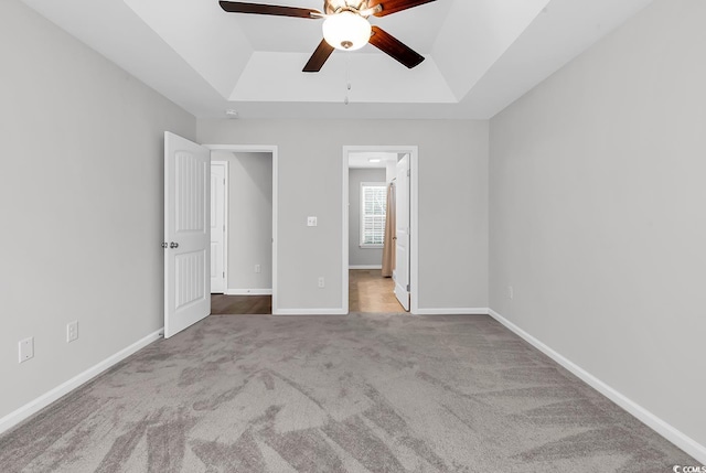 unfurnished bedroom featuring a tray ceiling, carpet, baseboards, and a ceiling fan