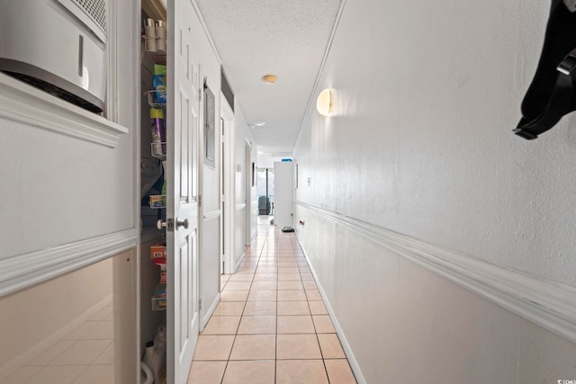 corridor featuring light tile patterned floors, baseboards, and a textured ceiling