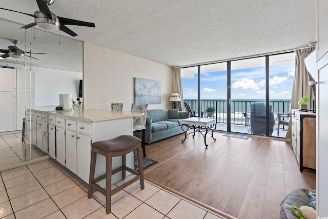 living area with a textured ceiling, floor to ceiling windows, ceiling fan, and a water view
