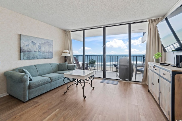 living area with floor to ceiling windows, light wood-style flooring, plenty of natural light, and a textured ceiling