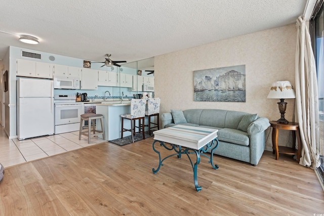 living room featuring a textured ceiling, light wood-style flooring, and ceiling fan