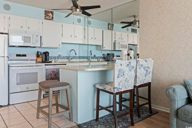kitchen with white appliances, a ceiling fan, a textured ceiling, a breakfast bar area, and white cabinets