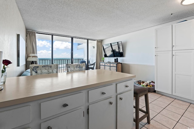 kitchen featuring a textured ceiling, floor to ceiling windows, light tile patterned flooring, light countertops, and white cabinets