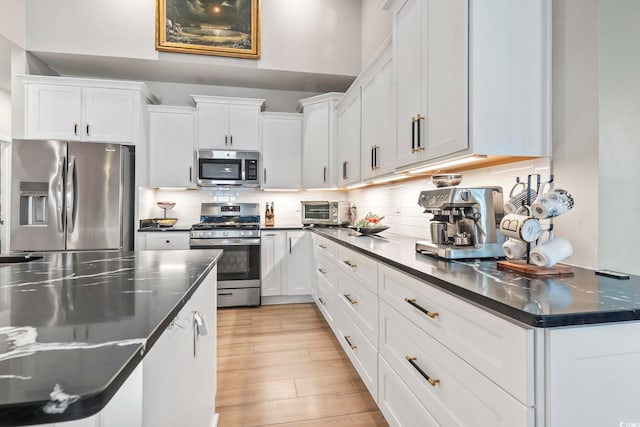 kitchen with stainless steel appliances, dark countertops, and white cabinets