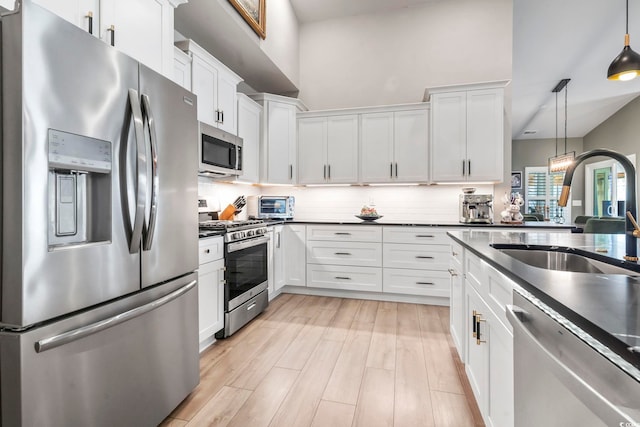 kitchen with appliances with stainless steel finishes, a sink, dark countertops, and white cabinets
