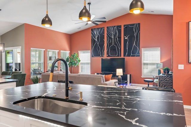kitchen with a sink, vaulted ceiling, dark countertops, white cabinetry, and a ceiling fan