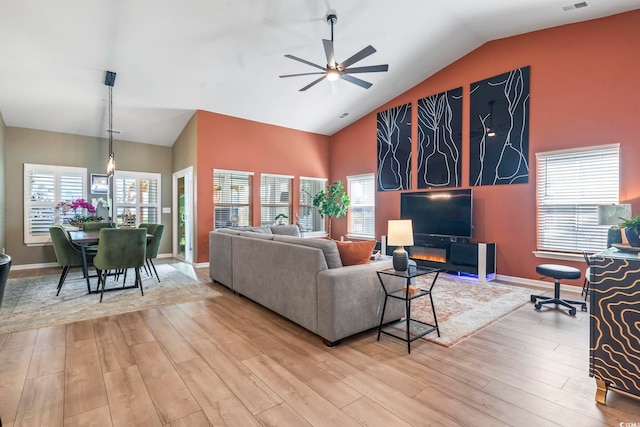 living area featuring a ceiling fan, high vaulted ceiling, light wood finished floors, and baseboards