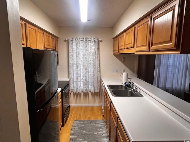 kitchen featuring black appliances, a sink, light wood finished floors, and brown cabinets