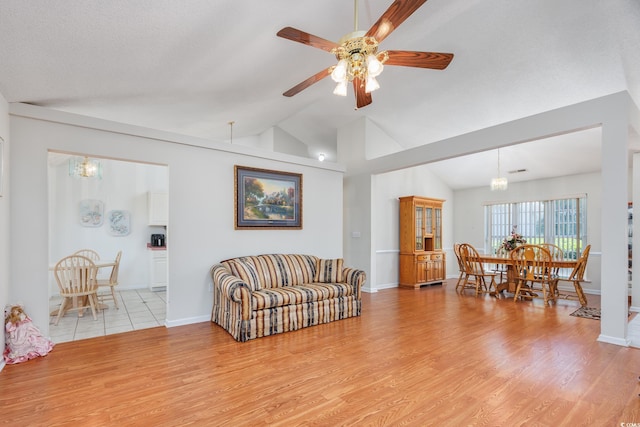 living room featuring a chandelier, light wood finished floors, vaulted ceiling, ceiling fan, and baseboards
