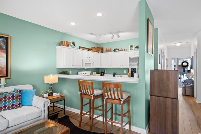 1058 Sea Mountain Hwy Unit 9-101, North Myrtle Beach, SC 29582 - kitchen with white microwave, stainless steel refrigerator with ice dispenser, a breakfast bar, white cabinets, and light wood-style flooring