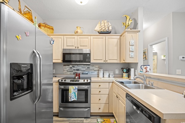 kitchen featuring stainless steel appliances, a sink, light brown cabinetry, light countertops, and a textured ceiling