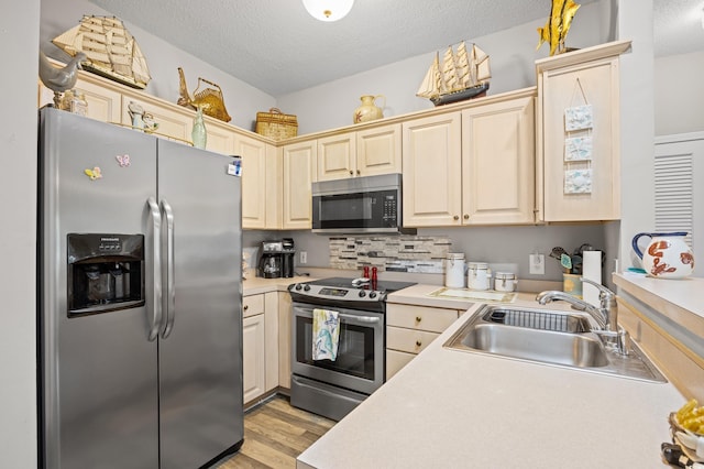 kitchen with appliances with stainless steel finishes, a sink, light countertops, a textured ceiling, and light wood finished floors