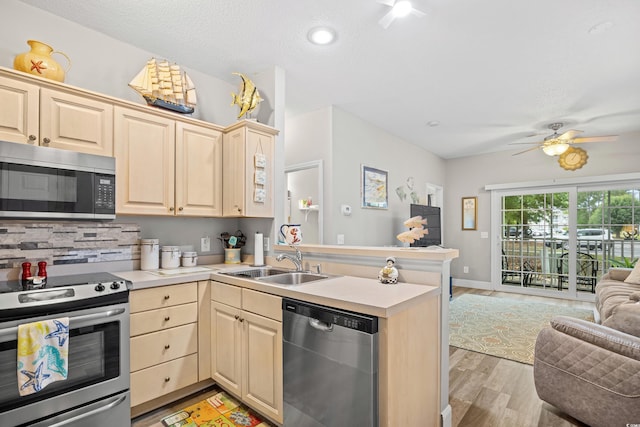 kitchen featuring stainless steel appliances, open floor plan, a sink, a peninsula, and light wood-style floors