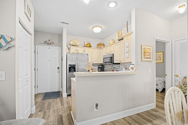 kitchen featuring appliances with stainless steel finishes, light wood-type flooring, a peninsula, a textured ceiling, and light countertops