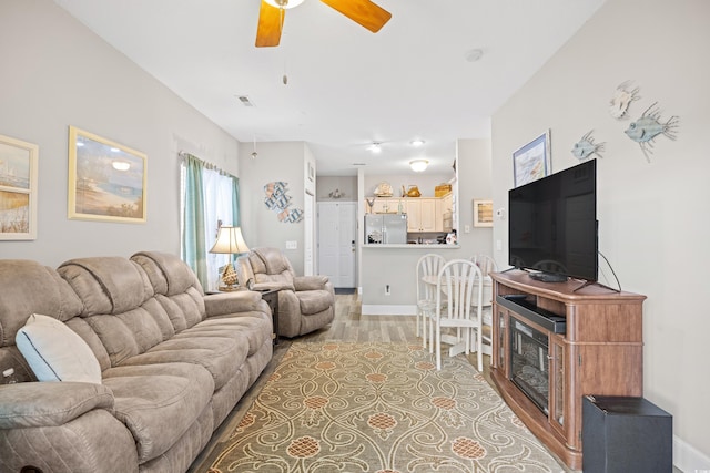 living room featuring ceiling fan, light wood-style floors, and baseboards