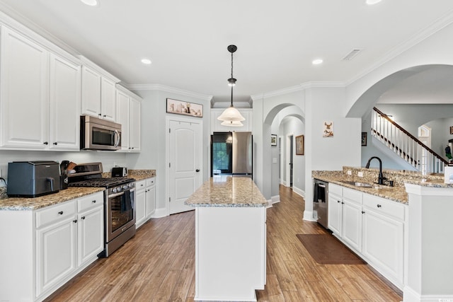 kitchen with appliances with stainless steel finishes, a sink, a center island, arched walkways, and light wood-style floors