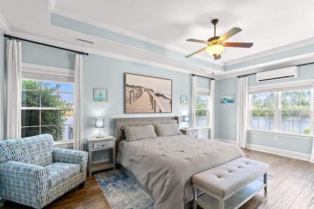 bedroom with a tray ceiling, a wall unit AC, crown molding, wood finished floors, and baseboards