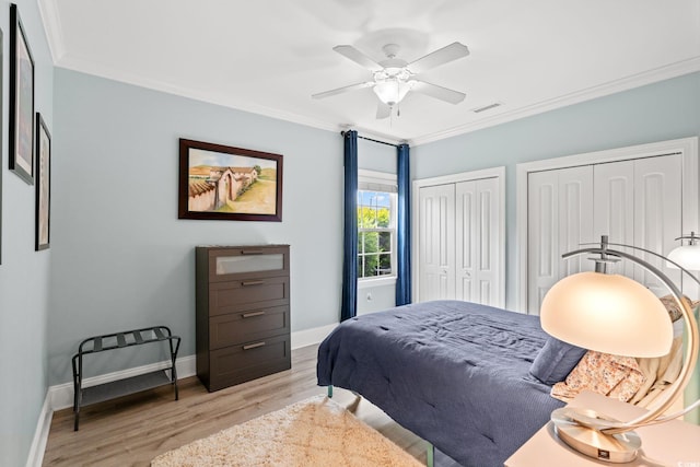 bedroom with two closets, crown molding, light wood finished floors, baseboards, and a ceiling fan