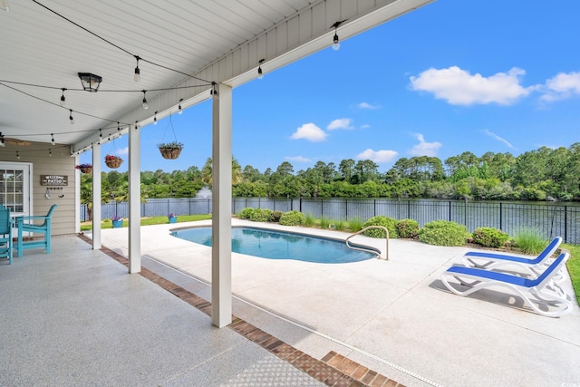 view of swimming pool featuring a patio, a water view, a fenced backyard, ceiling fan, and view of scattered trees