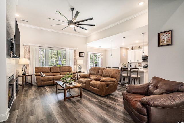 living room with a large fireplace, ceiling fan, dark wood-style flooring, ornamental molding, and recessed lighting