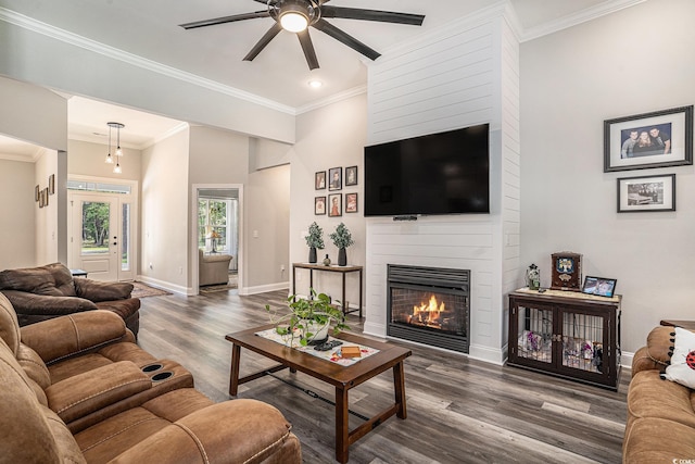 living room featuring a large fireplace, ceiling fan, wood finished floors, baseboards, and crown molding