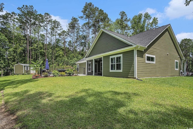 rear view of house with an outdoor structure, a lawn, a storage unit, and roof with shingles