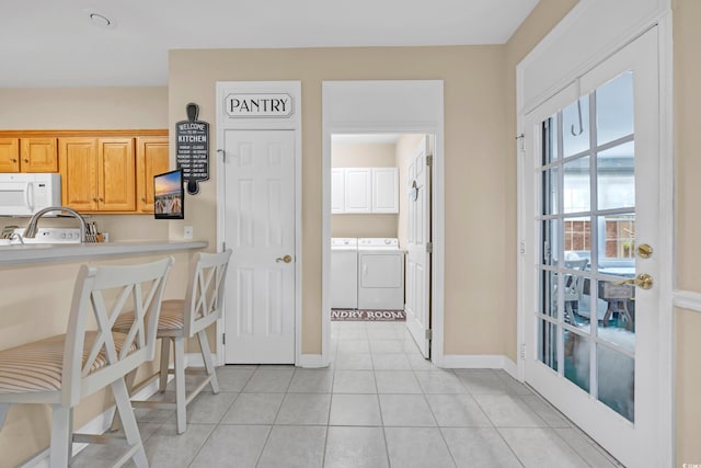 3071 Alice Ln, Little River, SC 29566 - kitchen with white microwave, washing machine and clothes dryer, light countertops, light tile patterned floors, and a kitchen bar