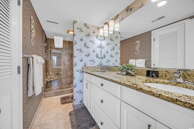 bathroom with a stall shower, double vanity, tile patterned flooring, a textured ceiling, and baseboards