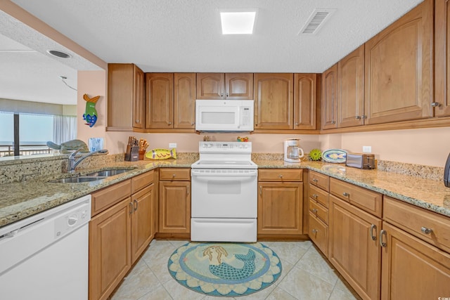 kitchen featuring white appliances, a sink, light stone countertops, brown cabinetry, and a textured ceiling