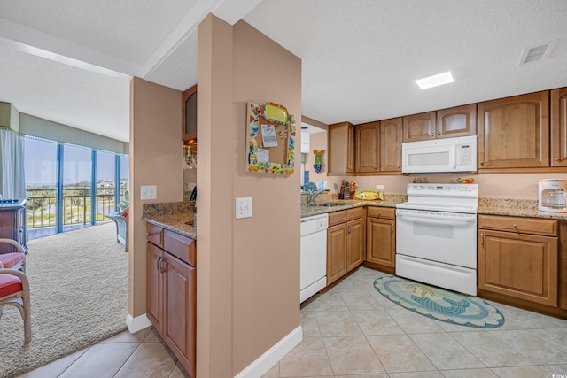 kitchen with white appliances, light tile patterned floors, light stone counters, brown cabinetry, and a textured ceiling