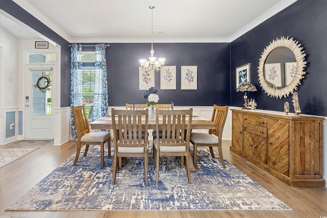 dining area featuring a chandelier, wood finished floors, wainscoting, a decorative wall, and crown molding