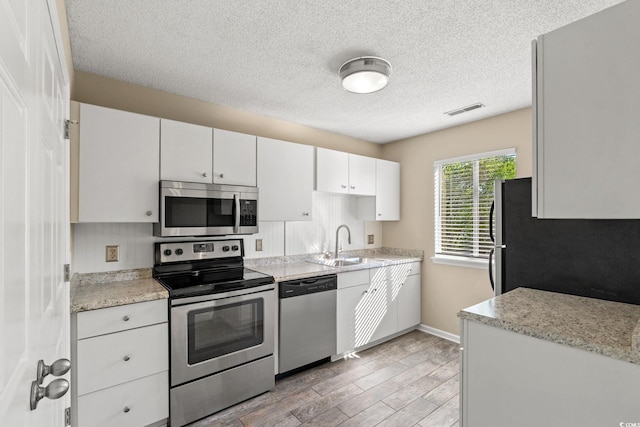 kitchen featuring stainless steel appliances, a sink, a textured ceiling, light wood-type flooring, and white cabinetry
