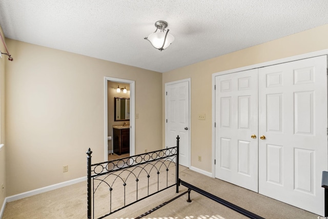 bedroom with light colored carpet, a closet, baseboards, a textured ceiling, and connected bathroom
