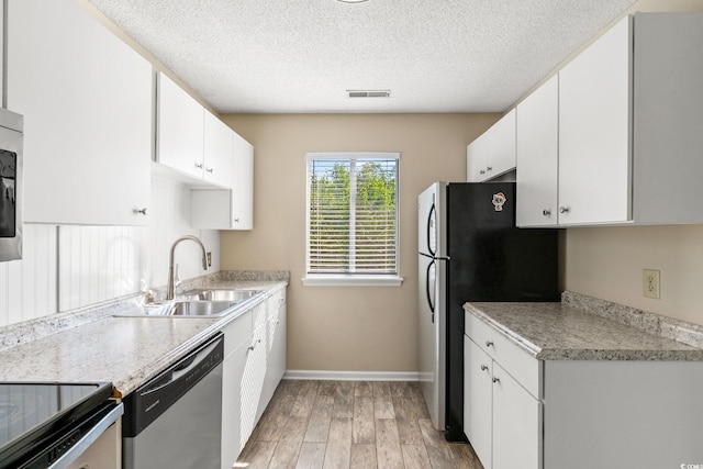 kitchen featuring a sink, appliances with stainless steel finishes, light wood-type flooring, baseboards, and a textured ceiling