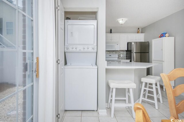 404 1st Ave N Unit H, North Myrtle Beach, SC 29582 - kitchen with white appliances, stacked washer / drying machine, light tile patterned floors, a kitchen bar, and white cabinetry