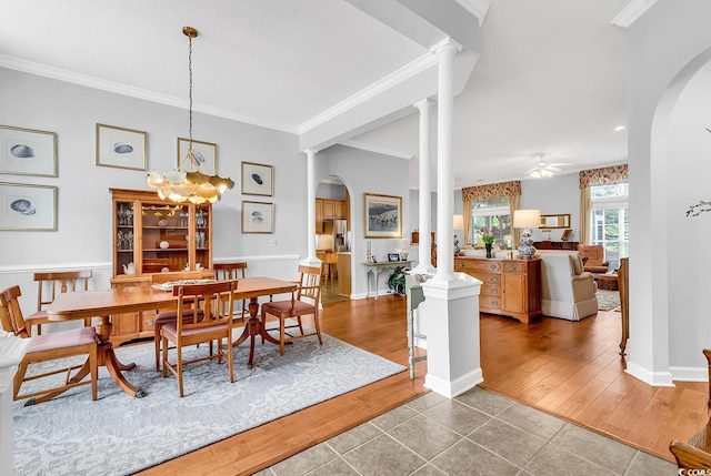 tiled dining space featuring arched walkways, ornamental molding, a ceiling fan, and a chandelier