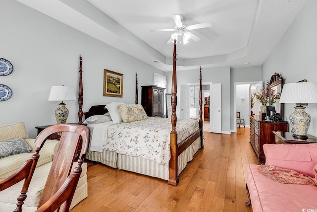 bedroom featuring light wood-style floors, a raised ceiling, baseboards, and ceiling fan