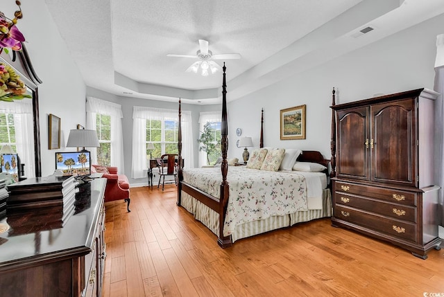 bedroom with light wood-style floors, a textured ceiling, and a raised ceiling