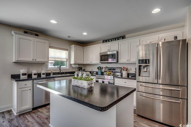 kitchen featuring stainless steel appliances, a sink, dark countertops, wood finished floors, and recessed lighting