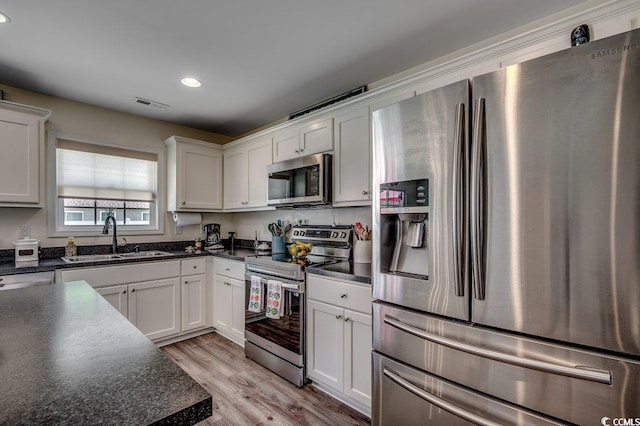 kitchen featuring stainless steel appliances, a sink, dark countertops, recessed lighting, and light wood finished floors