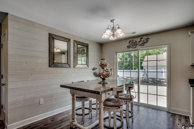 dining space with wood walls, a chandelier, baseboards, and dark wood-type flooring