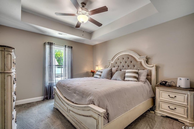 carpeted bedroom with a raised ceiling, baseboards, and a ceiling fan