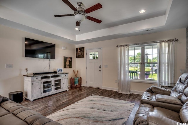 living area with a tray ceiling, ceiling fan, dark wood finished floors, recessed lighting, and baseboards
