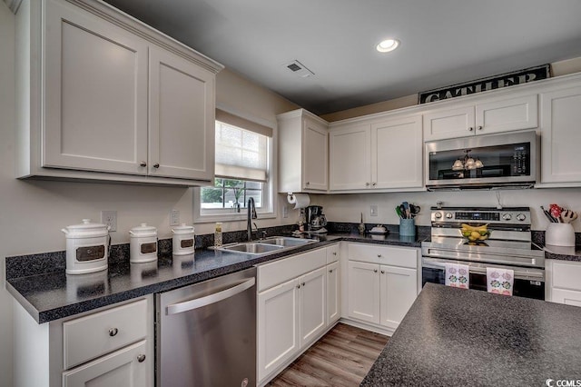 kitchen with appliances with stainless steel finishes, a sink, dark countertops, white cabinetry, and recessed lighting