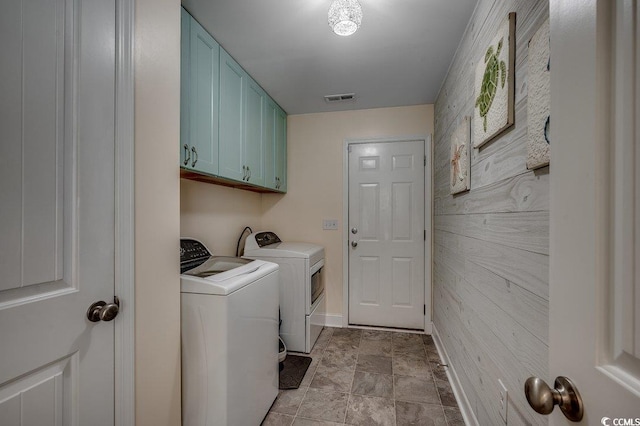 washroom featuring cabinet space, washing machine and dryer, baseboards, an accent wall, and stone finish floors