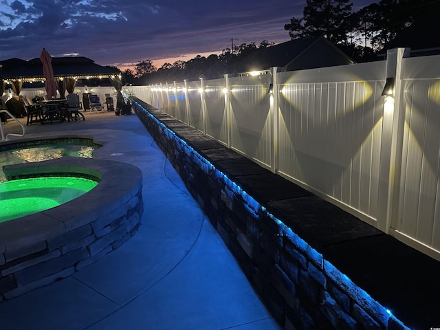pool at dusk with an in-ground hot tub, a patio area, a gazebo, and fence