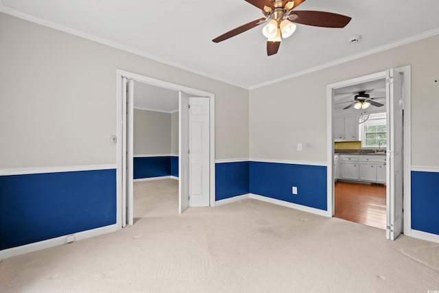 unfurnished room featuring light colored carpet, ceiling fan, crown molding, baseboards, and a sink