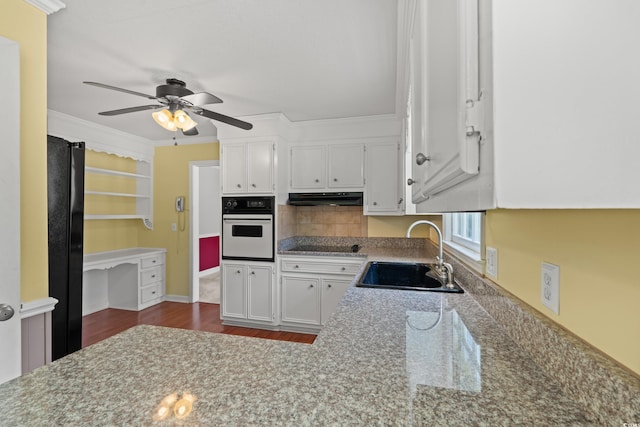 kitchen with oven, a sink, under cabinet range hood, ceiling fan, and white cabinets
