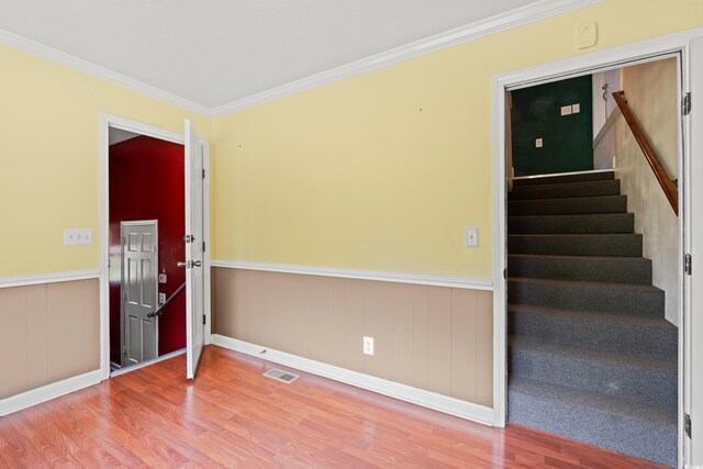 empty room with wood finished floors, ornamental molding, a wainscoted wall, stairway, and baseboards